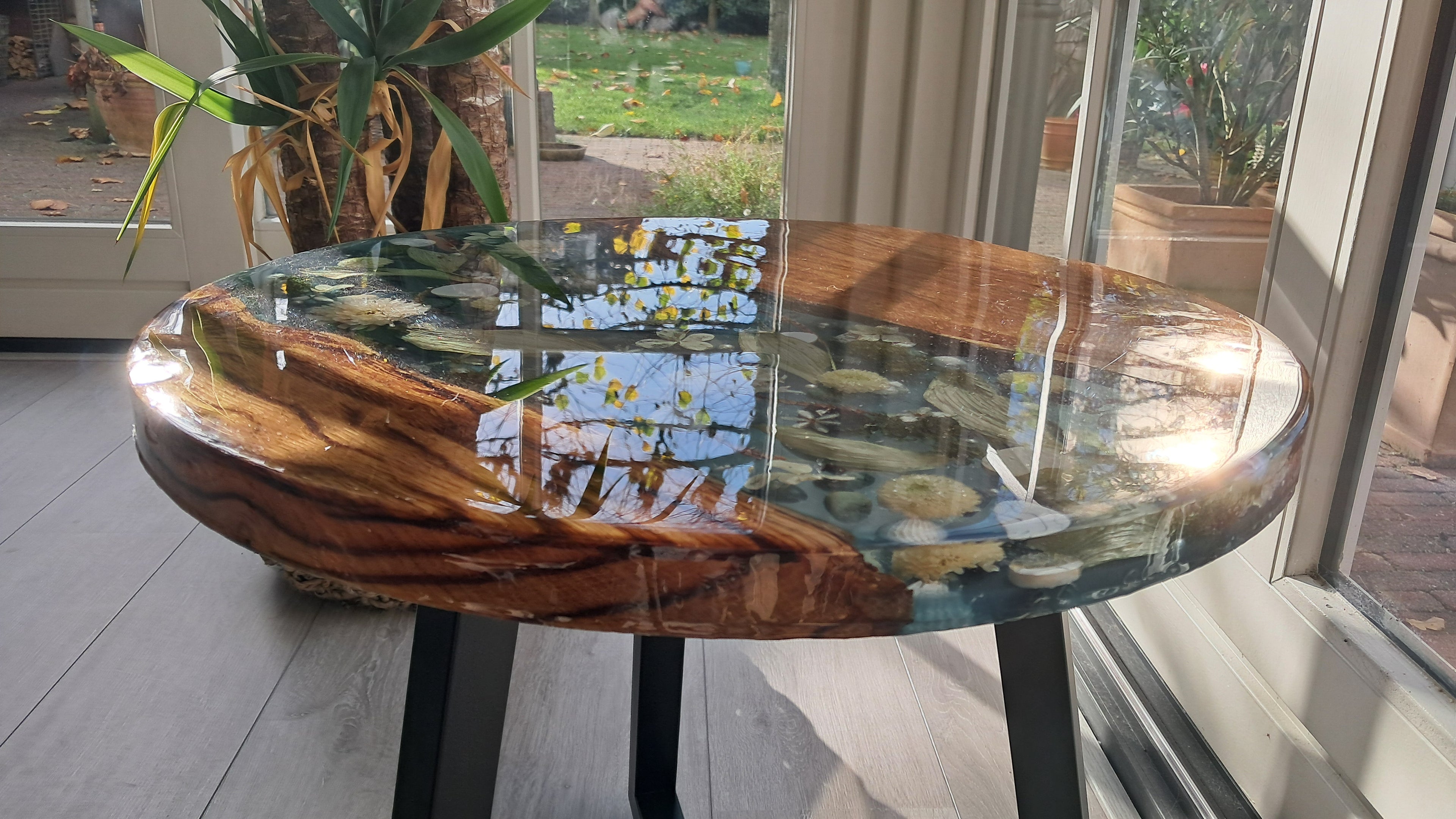 Handgemaakte Epoxy tafel Rivier met unieke uitstraling, houten basis en decoratieve elementen.